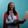 Young professional woman wearing cape, smiling and holding a computer.