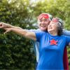 Retired couple outside smiling, with arms outstretched and wearing hero capes