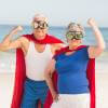 Retired couple wearing hero capes standing on the beach.
