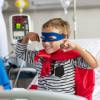 Boy in hospital bed smiling with super hero costume on